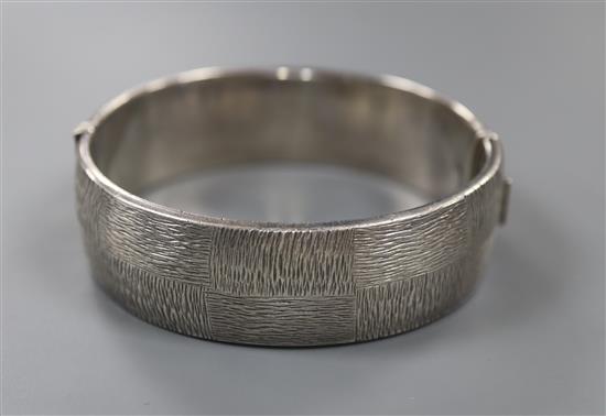 A 1970s textured silver hinged bracelet, with checkered decoration, by Rigby & Wilson, gross 46 grams.